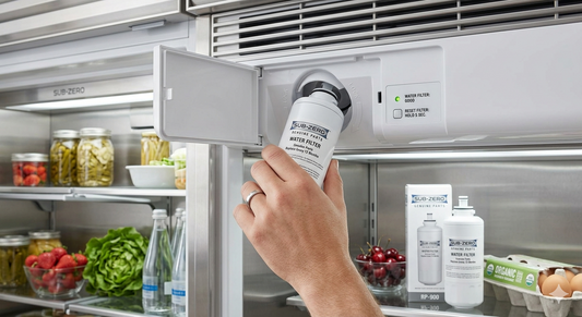 A close-up view inside a Sub-Zero refrigerator showing a hand inserting a white water filter cartridge into its housing near the top grille.